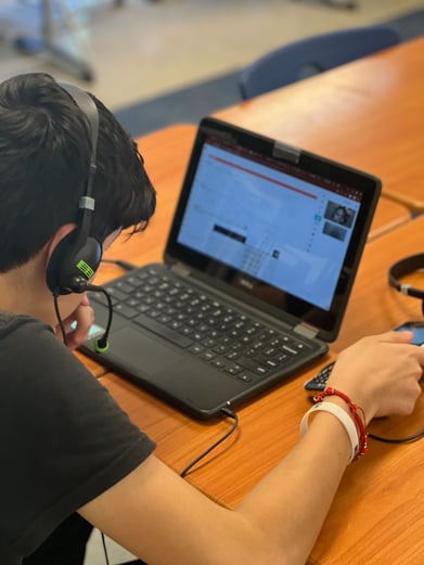 Student with headphones working on their calculator and looking at their laptop to solve a math problem