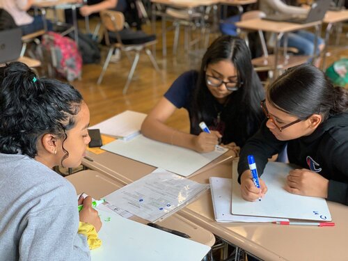 Tutor sitting at the desk with two students working together on math problems